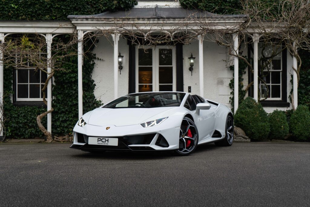 White Lamborghini Huracán Spyder hire parked in front of an elegant manor house, showcasing its sleek design and red brake calipers.